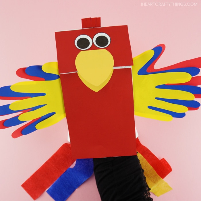 Adult with their hand inside the paper bag parrot puppet showing how to move the beak open and closed.