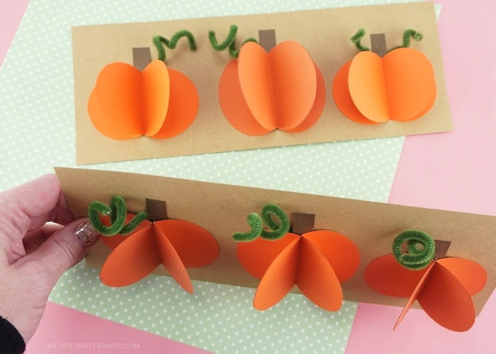 Two paper pumpkin crafts with adult holding one up to see a downward angle of the 3d pumpkins.