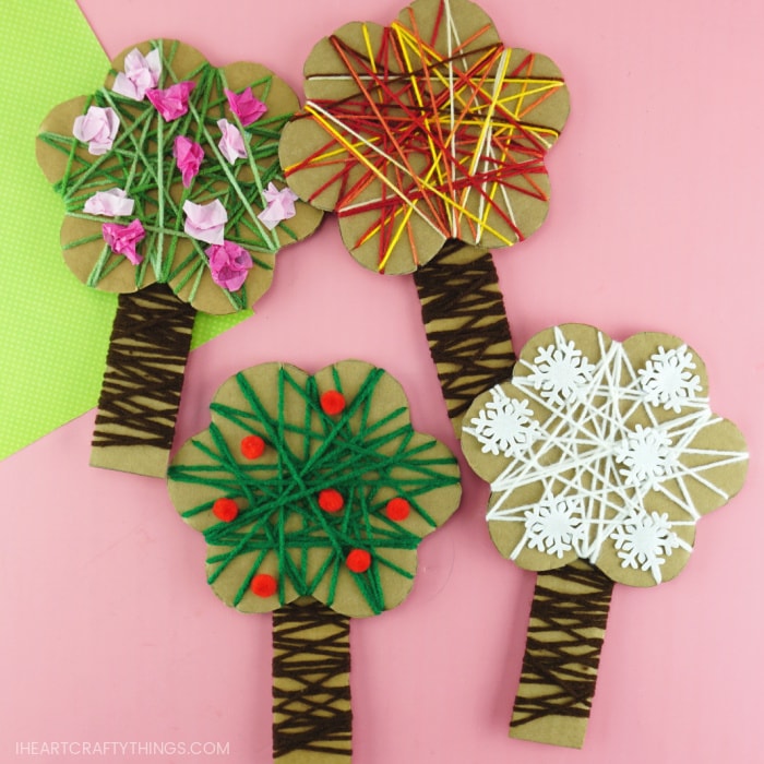 Close up square image of spring, summer, fall and winter yarn wrapped trees laying flat on a pink background.