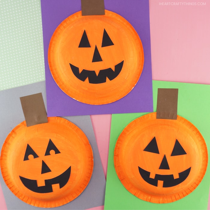 Square image showing three completed paper bowl pumpkin crafts laying with each other on a pink background.