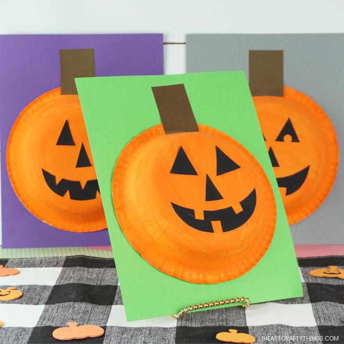 Paper bowl pumpkin craft propped up on an angle in center with two more pumpkin crafts out of focus in the background.