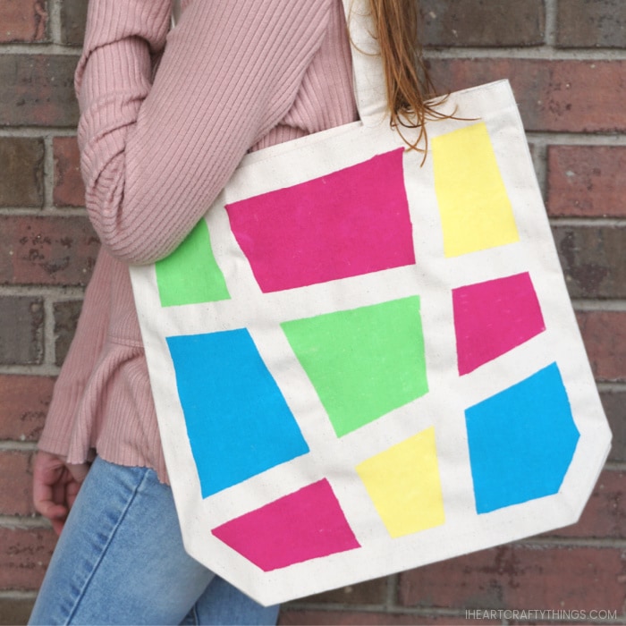 A girl standing sideways with the geometric painted canvas bag over her shoulder.