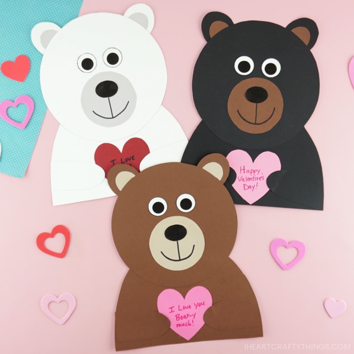Polar bear, black bear and brown bear Valentine Craft all touching and laying next to each other on a pink background with hearts scattered around.