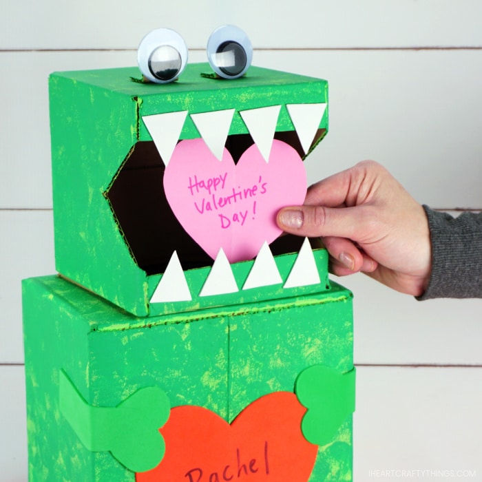 Close up image of person placing a heart Valentine inside the mouth of the dinosaur Valentine box.