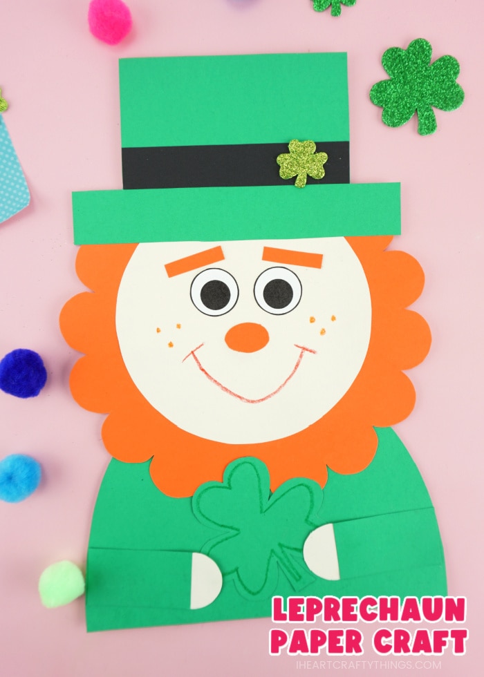 Close up vertical image of a leprechaun paper craft with colored poms scattered around it and the words "Leprechaun Paper Craft" in the bottom right corner.