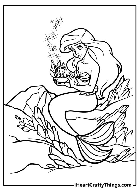 Coloring picture presenting Ariel sitting surrounded by rocks and holding a music box
